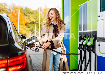 Beautiful woman filling car with gasoline at gas station. Online pay. Woman using app on phone. Beautiful woman filling car with gasoline at gas station. Online pay. Woman using app on phone. 137118434