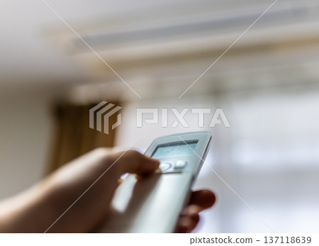 Hand to operate the remote control of the air conditioner 137118639