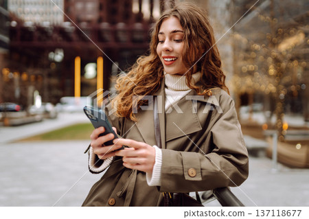 Happy female browsing internet in smartphone while standing on street. Lifestyle, travel, technology Happy female browsing internet in smartphone while standing on street. Lifestyle, travel, technology 137118677