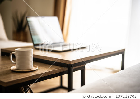 A laptop and a mug by a bright window 137118702
