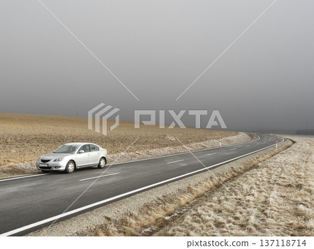 Silver car parked on a winding rural asphalt road through frosty farmland under dense winter fog, Silver car parked on a winding rural asphalt road through frosty farmland under dense winter fog, 137118714