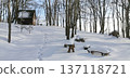 Snow-covered wooden cabin on a quiet forest hillside in winter, with footprints leading through fresh snow 137118721