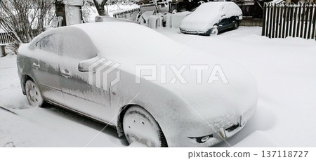 Snow-covered sedan parked in a residential driveway after heavy snowfall 137118727