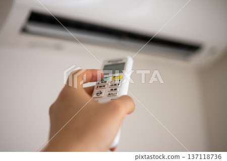 Hand to operate the remote control of the air conditioner 137118736
