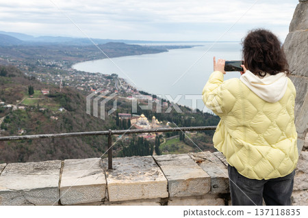 Female tourist photographing monastery landscape with smartphone from stone viewpoint overlooking New Athos and Black Sea coastline, Travel lifestyle concept showing mobile photography, tourism Female tourist photographing monastery landscape with smartphone from stone viewpoint overlooking New Athos and Black Sea coastline, Travel lifestyle concept showing mobile photography, tourism 137118835