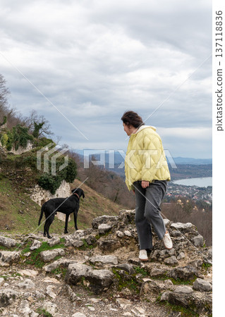 Woman stepping on stone ruins near black dog overlooking New Athos coastline and Black Sea from Anacopia fortress in Abkhazia under cloudy sky, Travel lifestyle scene suitable for tourism marketing Woman stepping on stone ruins near black dog overlooking New Athos coastline and Black Sea from Anacopia fortress in Abkhazia under cloudy sky, Travel lifestyle scene suitable for tourism marketing 137118836