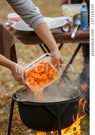 Adding vegetables to soup in outdoor cauldron Adding vegetables to soup in outdoor cauldron 137119159