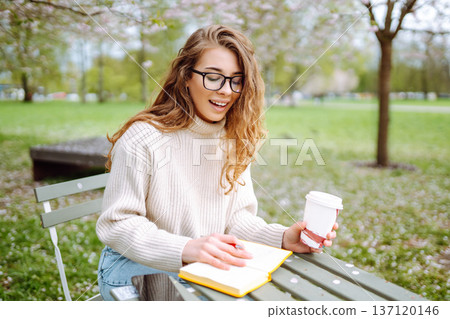 Happy woman relaxing in park, writing in notebook, sitting with laptop. Weekend, spring concept. Happy woman relaxing in park, writing in notebook, sitting with laptop. Weekend, spring concept. 137120146