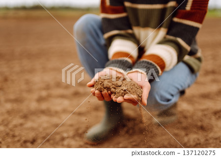 Young female farmer's hands touch dry soil in an agricultural field. Gardening and ecology concept. Young female farmer's hands touch dry soil in an agricultural field. Gardening and ecology concept. 137120275