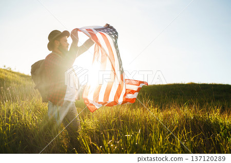 4th of July. American Flag.Patriotic holiday. Traveler with the flag of America. Beautiful sunset light. American style. 137120289