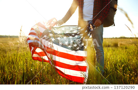 4th of July. American Flag. Traveler with the flag of America. The man in a hat, a backpack, a shirt and jeans. 137120290