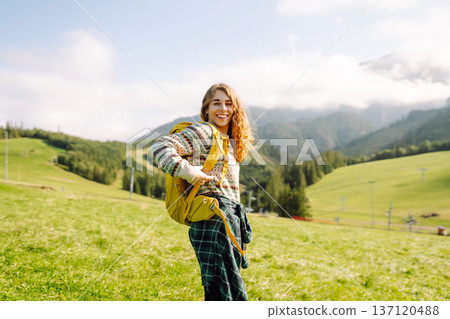 Female tourist with yellow backpack on top of mountain enjoying view of valley. Hiking concept. 137120488