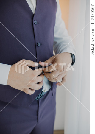 A man buttoning his vest near a window A man buttoning his vest near a window 137120567