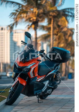 Modern sporty motorcycle parked on tropical city street with palm trees at sunset, Stylish urban motorbike standing on avenue in warm evening travel setting Modern sporty motorcycle parked on tropical city street with palm trees at sunset, Stylish urban motorbike standing on avenue in warm evening travel setting 137120782