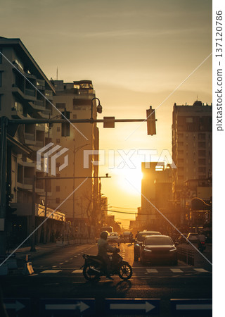 Golden sunset over Da Nang city street with motorbike silhouette, calm urban evening atmosphere, Warm golden hour light over Danang, peaceful city traffic scene with cars and scooter 137120786