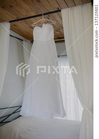 A wedding dress hangs above the bed A wedding dress hangs above the bed 137120801