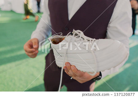 A groom with a shoe in his hands and alcohol in it A groom with a shoe in his hands and alcohol in it 137120877