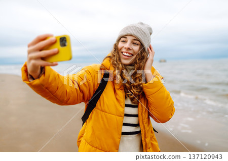 Portrait of young tourist in yellow jacket with phone in hands on seashore. Travel concept, blogging 137120943