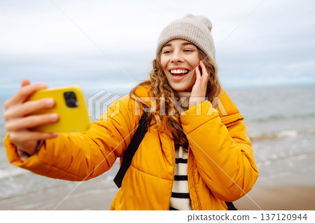 Portrait of young tourist in yellow jacket with phone in hands on seashore. Travel concept, blogging 137120944