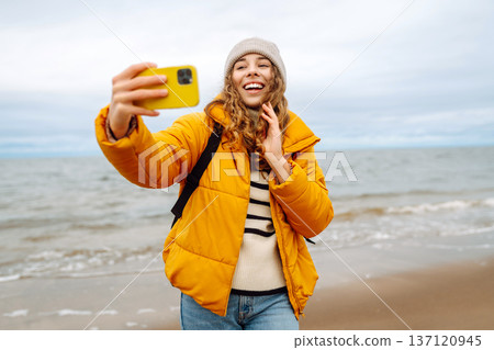 Portrait of young tourist in yellow jacket with phone in hands on seashore. Travel concept, blogging Portrait of young tourist in yellow jacket with phone in hands on seashore. Travel concept, blogging 137120945