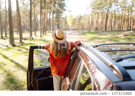 Young woman enjoying a sunny day by her car in forest setting during the afternoon. Summer trip Young woman enjoying a sunny day by her car in forest setting during the afternoon. Summer trip 137121060