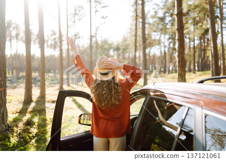 Young woman enjoying a sunny day by her car in forest setting during the afternoon. Summer trip Young woman enjoying a sunny day by her car in forest setting during the afternoon. Summer trip 137121061