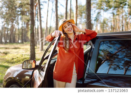 Young woman enjoying a sunny day by her car in forest setting during the afternoon. Summer trip Young woman enjoying a sunny day by her car in forest setting during the afternoon. Summer trip 137121063