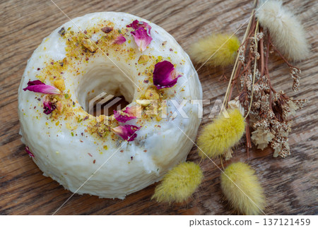 a Pistachio & Rose Baked Doughnuts featuring a white glaze and generous decoration of crushed pistachios and dried rose petals 137121459