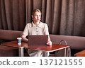 Confident business woman working on laptop indoors in modern cafe. Stylish female entrepreneur in elegant beige outfit, professional lifestyle, online business, remote work 137121555