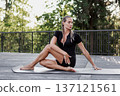 Fit woman practicing yoga with closed eyes outdoors on wooden deck in park. Athletic female in black sportswear sitting on mat in seated twist pose, flexibility and wellness concept 137121561
