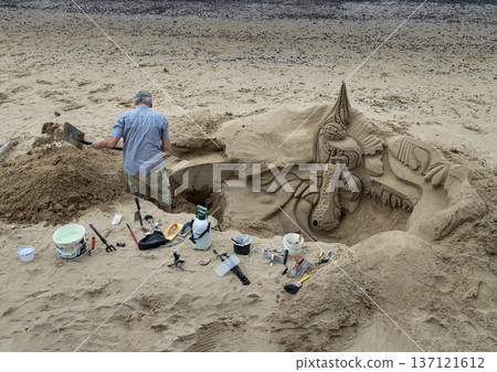 a sand artist at working on a detailed sand sculpture on a small beach. a sand artist at working on a detailed sand sculpture on a small beach. 137121612