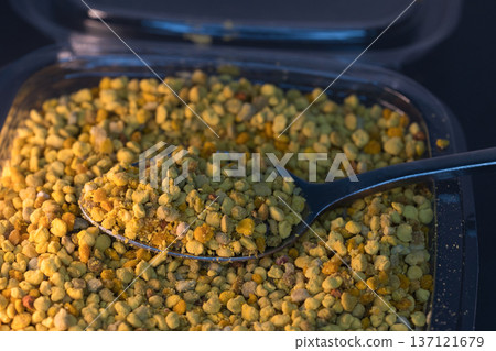 Close-up of natural bee pollen granules in vibrant yellow and orange tones, showcasing their organic texture.  137121679