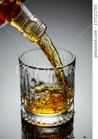 The amber-gold strong alcoholic beverage is poured into a glass. The amber-gold strong alcoholic beverage is poured into a glass. 137121703