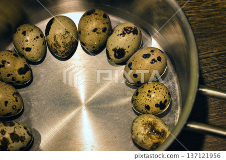 Top view of fresh speckled quail eggs arranged in a circle inside a metal bowl. Rustic food background showing organic farm produce, cooking ingredients, and healthy nutrition concept. 137121956