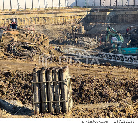 Reinforcement pile and construction workers inside excavation area under sunlight. Engineering groundwork, urban development, manual labor stage and building foundation progress. 137122155