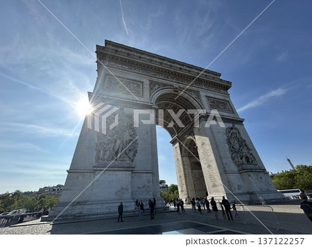 Low-angle view of the Arc de Triomphe in Paris shining under blue sky and sunlight 137122257