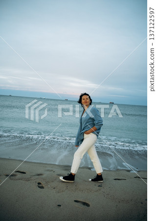 Woman Strolling Along Beach at Dusk Woman Strolling Along Beach at Dusk 137122597