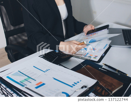 Auditors collaborating in modern office, analyzing financial documents and using calculator with a laptop displaying charts. Audit and taxes in business 137122744