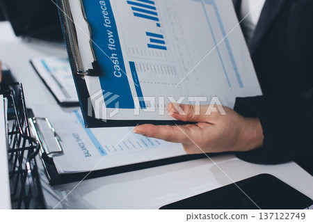 Auditors collaborating in modern office, analyzing financial documents and using calculator with a laptop displaying charts. Audit and taxes in business Auditors collaborating in modern office, analyzing financial documents and using calculator with a laptop displaying charts. Audit and taxes in business 137122749