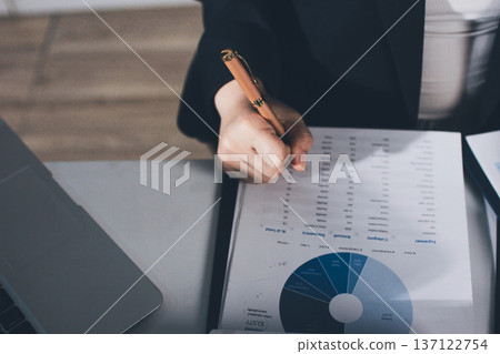 Auditors collaborating in modern office, analyzing financial documents and using calculator with a laptop displaying charts. Audit and taxes in business 137122754