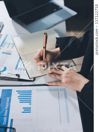 Auditors collaborating in modern office, analyzing financial documents and using calculator with a laptop displaying charts. Audit and taxes in business Auditors collaborating in modern office, analyzing financial documents and using calculator with a laptop displaying charts. Audit and taxes in business 137122758