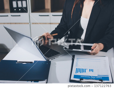 Auditors collaborating in modern office, analyzing financial documents and using calculator with a laptop displaying charts. Audit and taxes in business Auditors collaborating in modern office, analyzing financial documents and using calculator with a laptop displaying charts. Audit and taxes in business 137122763