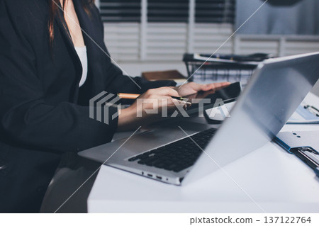 Auditors collaborating in modern office, analyzing financial documents and using calculator with a laptop displaying charts. Audit and taxes in business Auditors collaborating in modern office, analyzing financial documents and using calculator with a laptop displaying charts. Audit and taxes in business 137122764