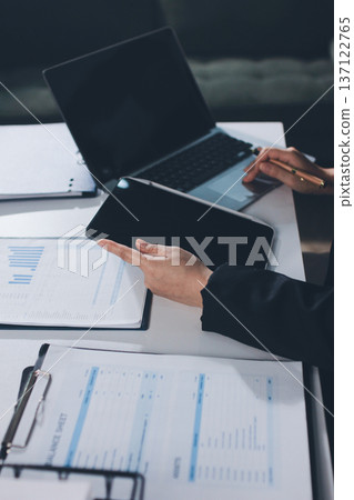 Auditors collaborating in modern office, analyzing financial documents and using calculator with a laptop displaying charts. Audit and taxes in business Auditors collaborating in modern office, analyzing financial documents and using calculator with a laptop displaying charts. Audit and taxes in business 137122765