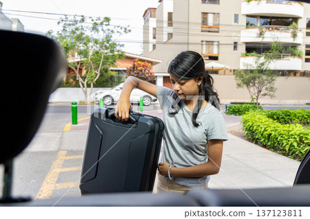 A teenager is holding a black suitcase and looking at it 137123811