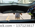 A teenager is standing in front of a car with a black trunk 137123817