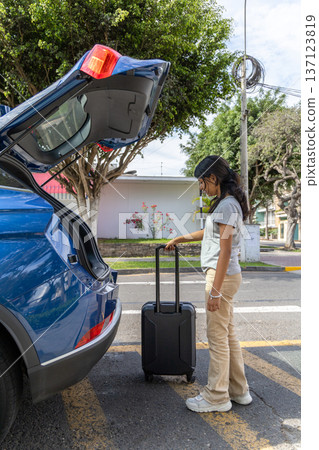 A teenager is standing next to a blue car with a suitcase in the trunk A teenager is standing next to a blue car with a suitcase in the trunk 137123819