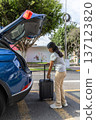 A teenager is getting ready to leave in a blue car with a suitcase in the trunk 137123820