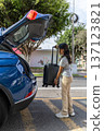 A teenager is pulling a suitcase out of the back of a blue car 137123821