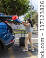 A teenager is pulling a suitcase out of the back of a blue car 137123826